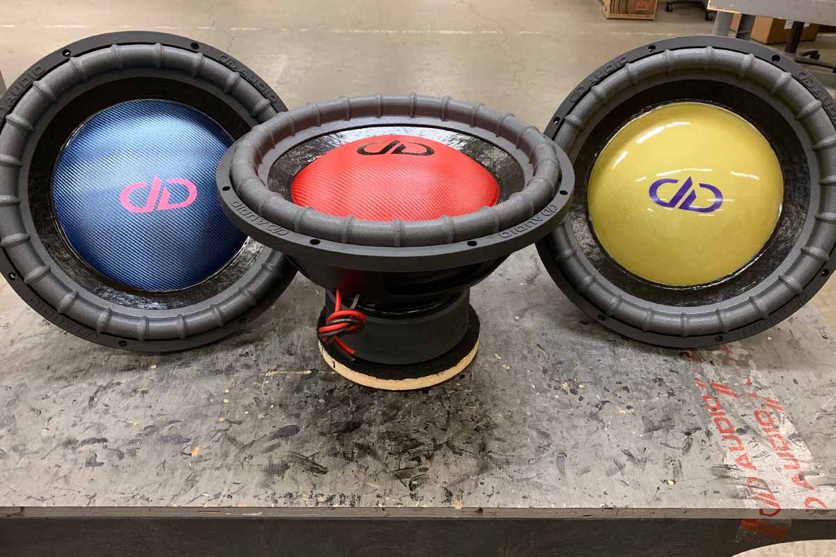 Three USA Made Subwoofers: left) blue dust cap with pink DDA logo, center) red dust cap with black DDA logo, right) yellow dust cap with Purple logo
